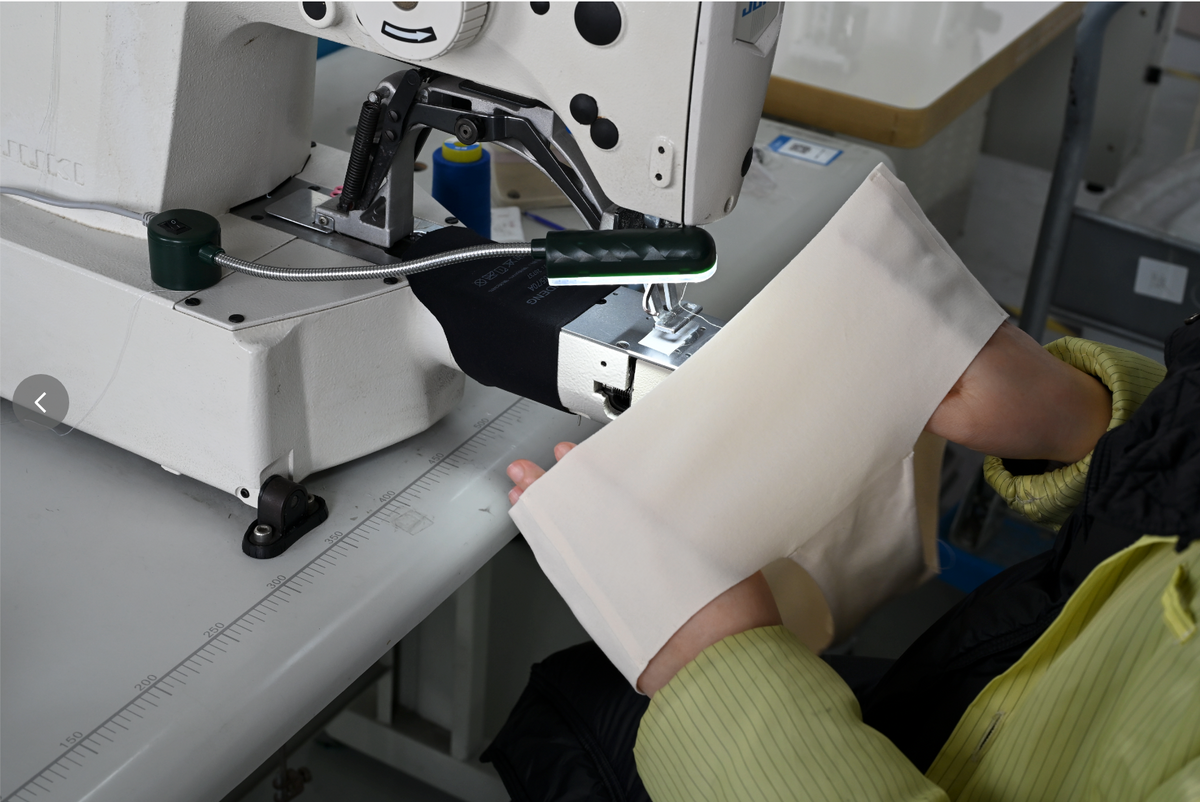 Hands inspecting a fabric sample at a sewing machine.