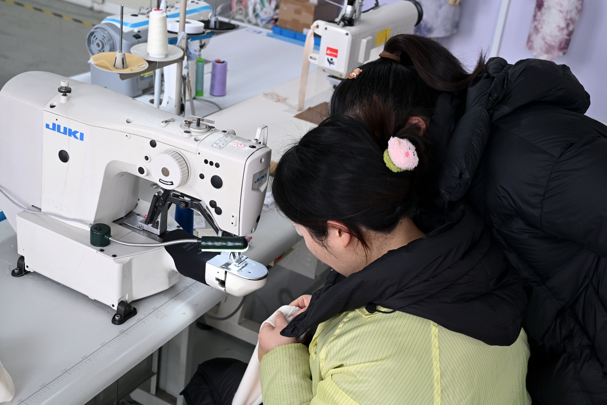 Two people working together at a sewing machine in the Shanghai workshop.